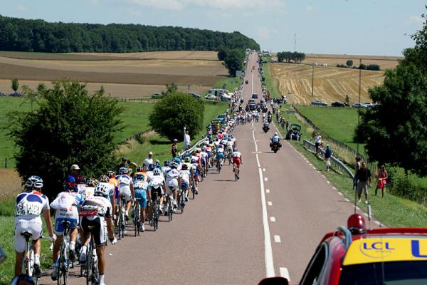 The peloton is stretched out along a long, straight road.